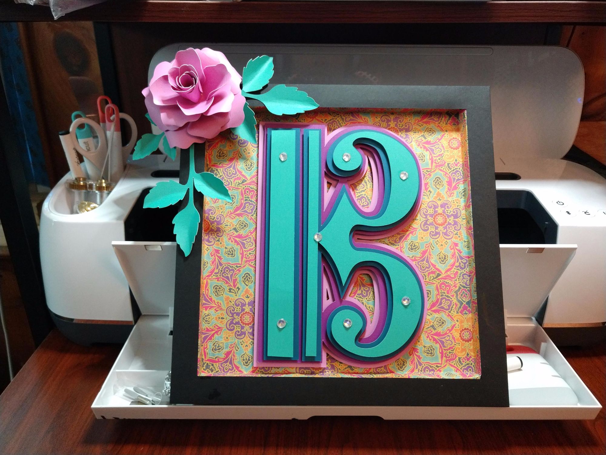 Alto clef within a frame in bright colors of teal, blue, purple, and pink, with a large pink flowers at upper left on frame