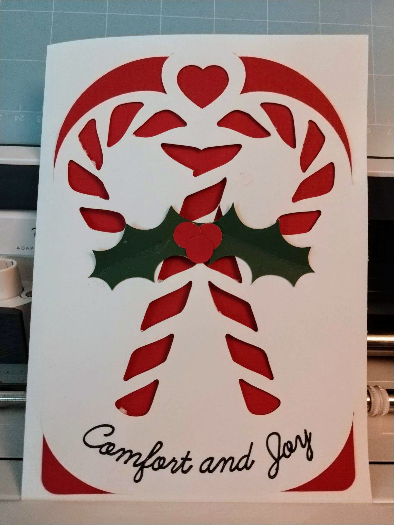 Two crossed candy canes with a sprig of holly in the center